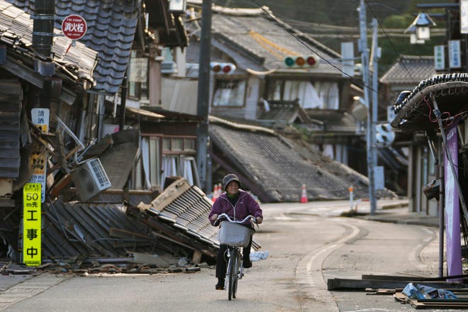 A woman bikes amid damaged houses in Noto town in the Noto peninsula facing the Sea of Japan, northwest of Tokyo, Tuesday, Jan. 2, 2024, following Monday's deadly earthquake. A series of powerful earthquakes that hit western Japan have damaged thousands of buildings, vehicles and boats. Officials warned that more quakes could lie ahead.