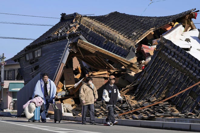 A man carries his belongings past a collapsed house following an earthquake in Wajima, Ishikawa prefecture, Japan Tuesday, Jan. 2, 2024
