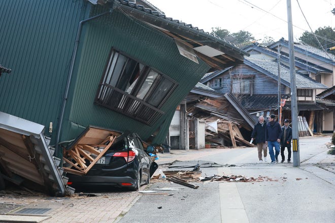 People walk past a badly damaged house in the city of Nanao, Ishikawa Prefecture, on January 2, 2024, a day after a major 7.5 magnitude earthquake struck the Noto region in Ishikawa prefecture.