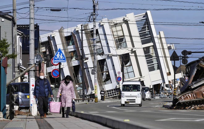 People make their way near a collapsed building due to an earthquake in Wajima, Ishikawa prefecture, Japan Tuesday, Jan. 2, 2024.