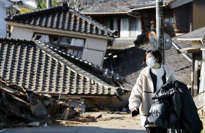 A woman walks in front of collapsed houses following earthquake in Noto-cho, Ishikawa prefecture, Japan Tuesday, Jan. 2, 2024.