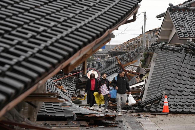 People make their way through fallen buildings in the earthquake-hit city of Suzu, Ishikawa prefecture, Japan, Wednesday, Jan. 3, 2024. A series of powerful earthquakes that hit western Japan left multiple people dead Wednesday as rescue workers fought to save those feared trapped under the rubble of collapsed buildings.