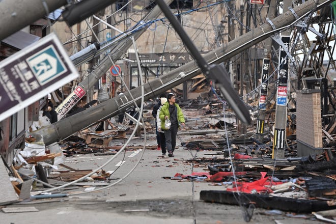 People walk past fallen utility poles and damaged buildings in the city of Wajima, Ishikawa prefecture on January 4, 2024, after a major 7.5 magnitude earthquake struck the Noto region in Ishikawa prefecture on New Year's Day. More than 50 people were reported missing on January 4 as Japanese rescuers battled to reach hundreds still cut off from help three days after a devastating earthquake left at least 78 dead.