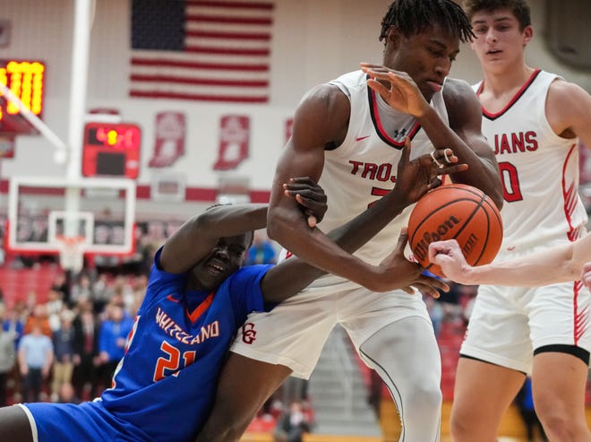 Whiteland's forward Akol Akol (21) falls while reaching for the ball against Center Grove Trojans forward Michael Ephraim (21) on Saturday, Jan. 13, 2024, during the Johnson County finals at Center Grove High School in Greenwood. The Center Grove Trojans defeated Whiteland, 68-43.