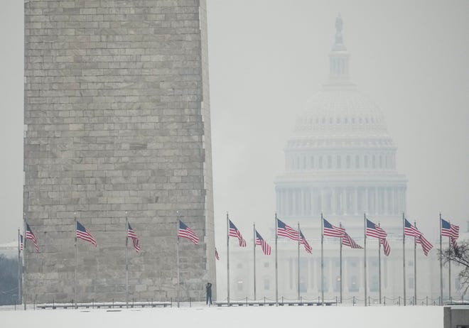People brave the elements at the Washington Memorial with the U.S. Capitol seen in the background after snow fell on the national Capitol overnight, accumulating anywhere from 2 to 5 inches in the region on Jan. 16, 2024.